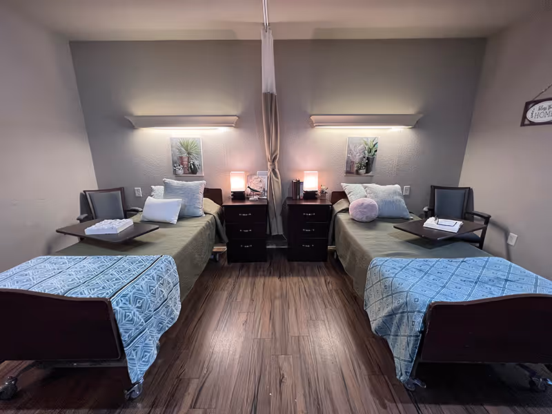 A shared bedroom with two twin beds separated by a central curtain, each with bedside tables, lamps, chairs, and decorative pillows.