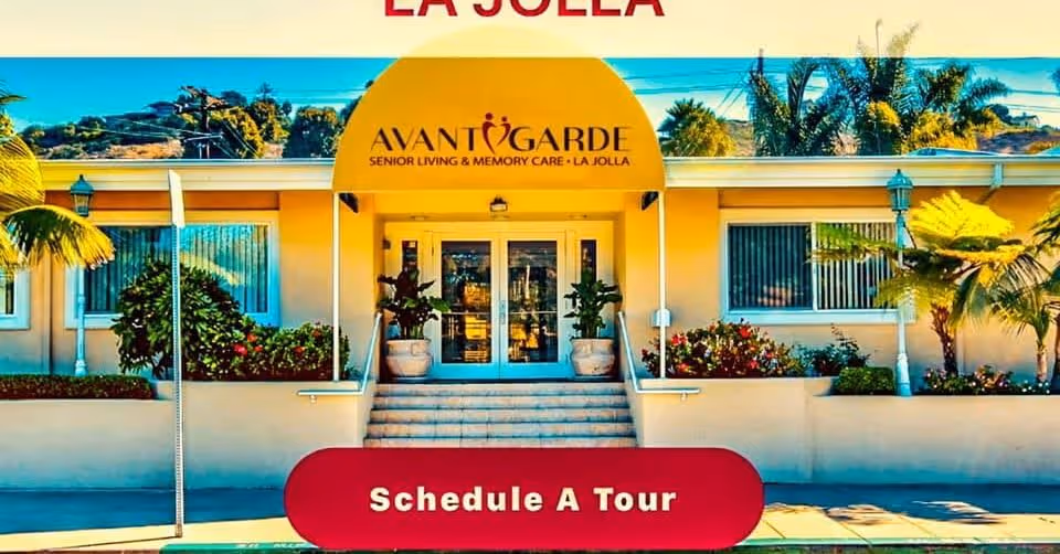 Front entrance of Avantgarde Senior Living La Jolla with a yellow awning, steps, potted plants, and a red "Schedule A Tour" banner.