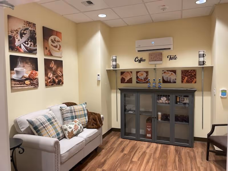 Cozy seating area with a loveseat, plaid pillows, coffee-themed wall art and a cabinet labeled 'Coffee Time'.