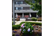 Front entrance of Teresian House Center for the Elderly with landscaped flowerbeds and benches in front of a multi-story building.