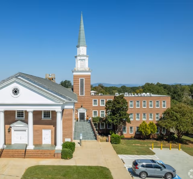 Exterior of Serene Haven Apartments: brick complex with a tall steeple, front stairs, and parking.