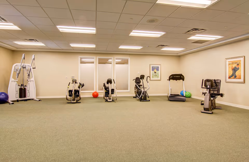 Empty fitness room with cardio machines, a treadmill and exercise balls against a beige wall.