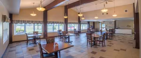 Bright dining hall with several tables, chairs, and large windows along the wall.