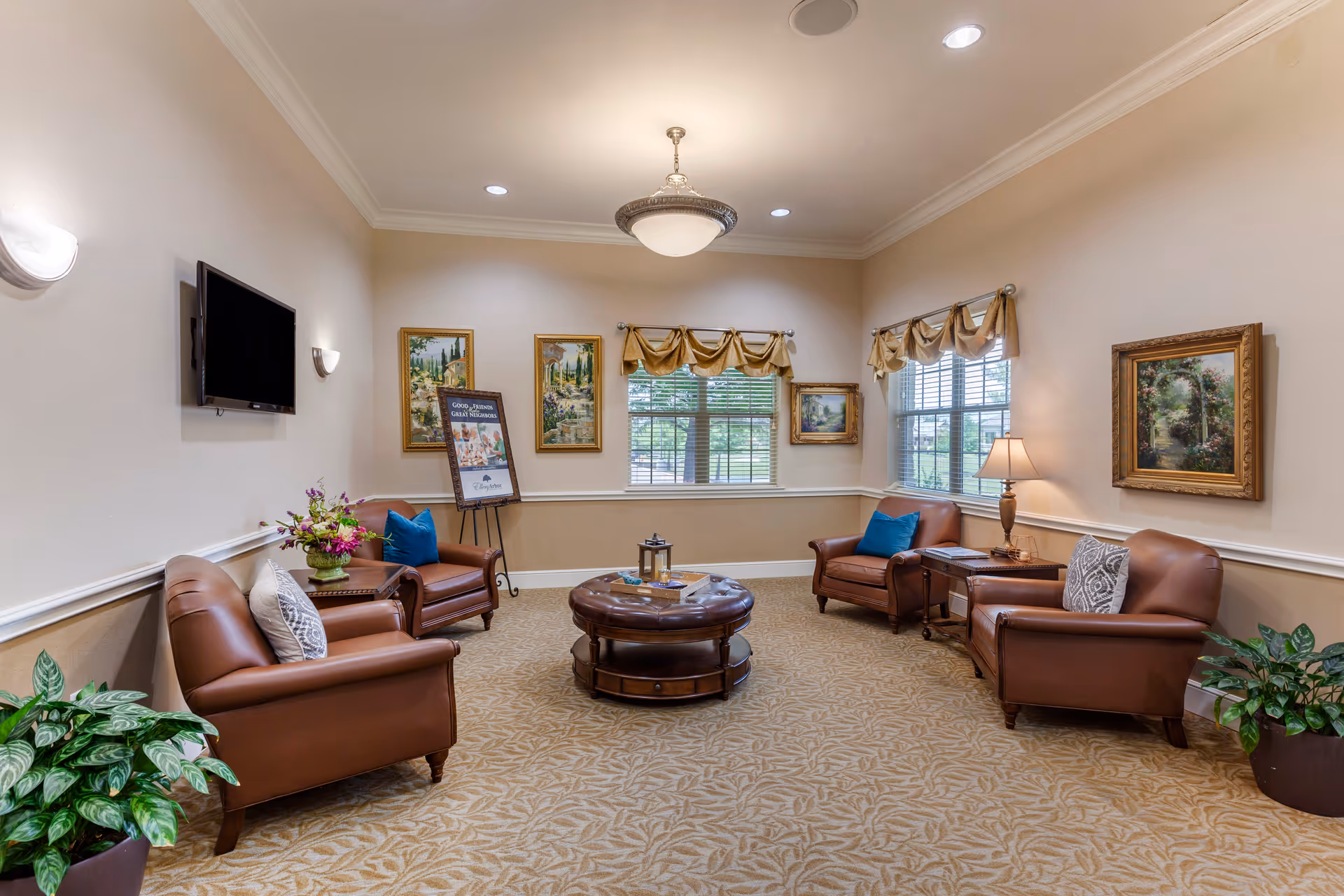 A cozy sitting room with leather armchairs arranged around a round coffee table, framed artwork, and windows with valances.