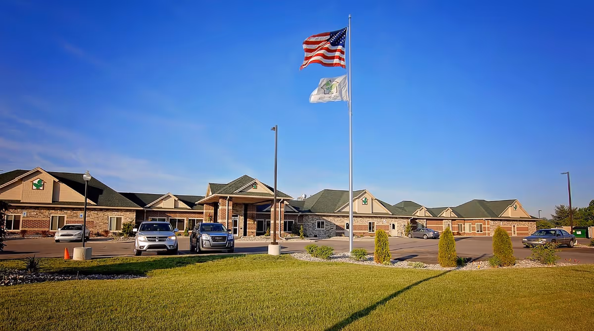 Exterior view of Bavarian Comfort Care facility with flagpoles, parking lot, and landscaping.