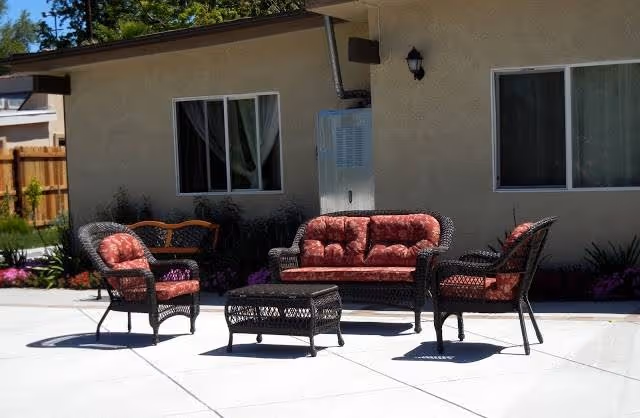 Wicker patio furniture with red cushions arranged on a concrete patio in front of a single-story building.