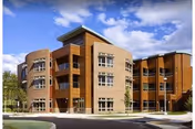 Exterior view of a modern three-story senior living facility building with a combination of brick and wood paneling under a partly cloudy blue sky.