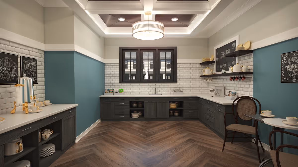 A modern kitchen area with dark wood cabinets, white countertops, and white subway tile backsplash. The walls are painted teal on the lower half and white on the upper half. There is a large window above the sink, a round ceiling light fixture, and two small tables with chairs on the right side. Various kitchen items and cups are neatly arranged on the counters and shelves.