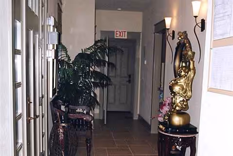 Hallway interior of a senior living facility with a plant, statue on pedestal, and seating.