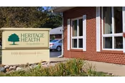 Brick-faced healthcare building exterior with windows, landscaping, and a large 'Heritage Health' sign by the entrance.