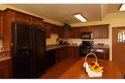 Spacious kitchen with dark wood cabinets, black refrigerator and oven, and a central wooden island topped with a basket of fruit.