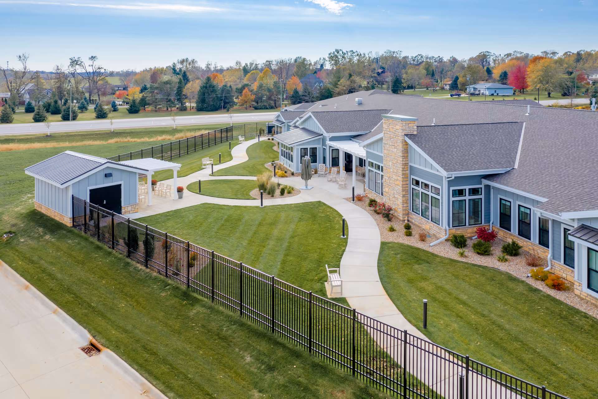 Aerial view of a single-story senior living facility with a curved walkway, landscaped lawn, and outdoor seating areas.