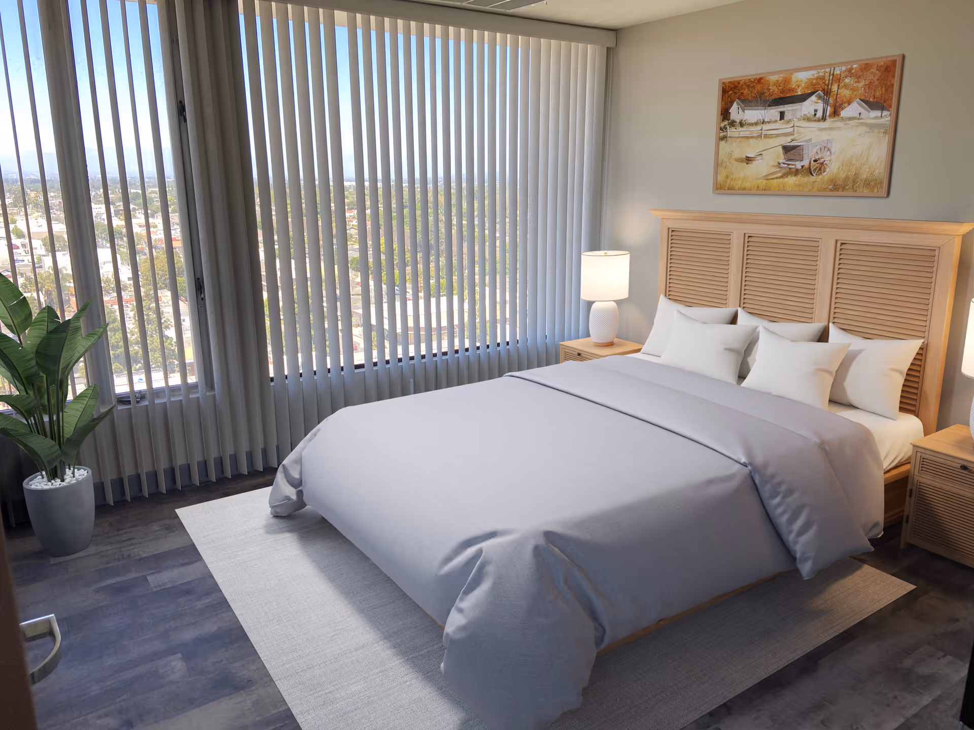 A bright bedroom with a large bed covered in light gray bedding and multiple white pillows. The room features wooden nightstands with white lamps on each side of the bed. A large window with vertical blinds offers a view of a cityscape outside. There is a potted plant in the corner and a framed painting of a rural scene with a house and autumn trees hanging above the bed.