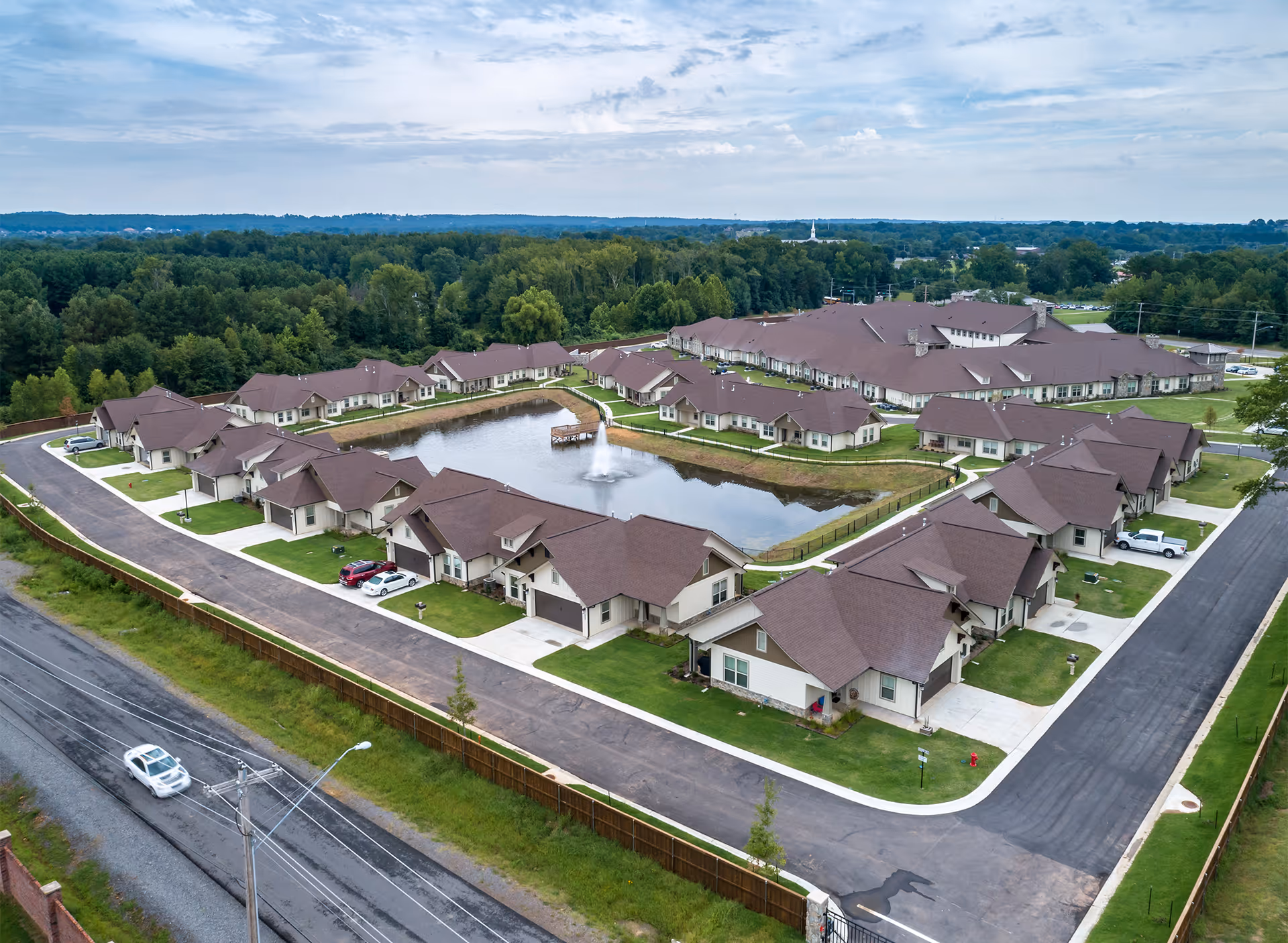 Aerial view of a senior living community with single-story cottages arranged around a central pond with a fountain.
