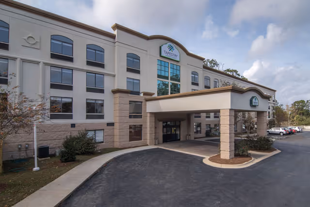 Exterior front view of Tapestry Senior Living Lakeshore building with a covered entrance and parking area on the right side under a partly cloudy sky.