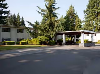 Exterior view of a senior living facility entrance with a carport and trees.