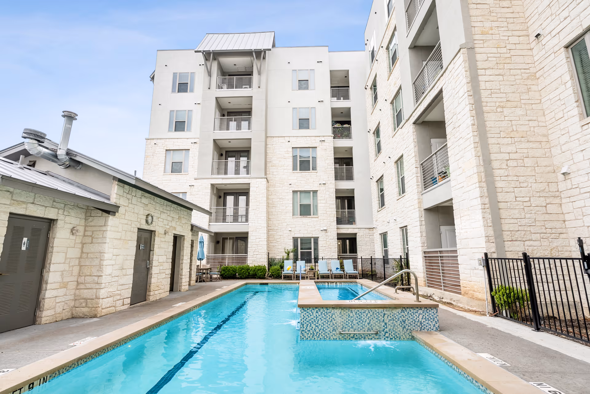 Outdoor courtyard pool and spa in front of a multi-story stone and stucco senior living building with balconies.