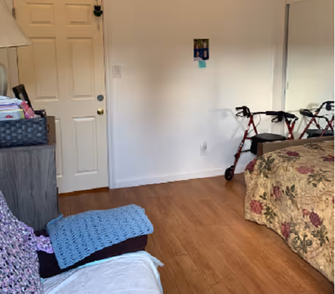 Bedroom with floral bedspread, walker, dresser, and door visible.