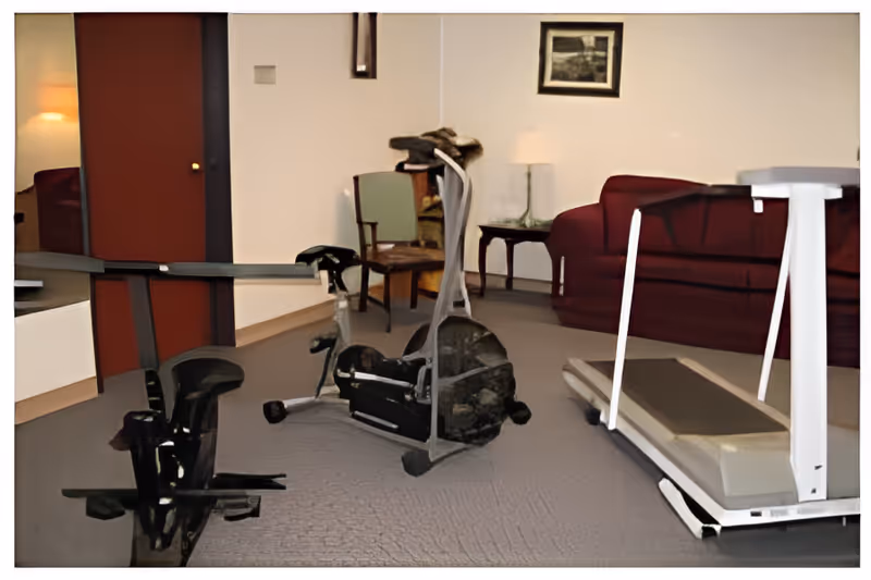 Interior common room with exercise equipment including a treadmill and stationary bikes, plus seating and a lamp.