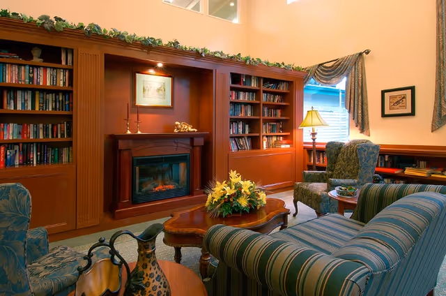 Cozy living room with built-in bookshelves and a fireplace, upholstered chairs and a striped sofa around a coffee table with a floral centerpiece.