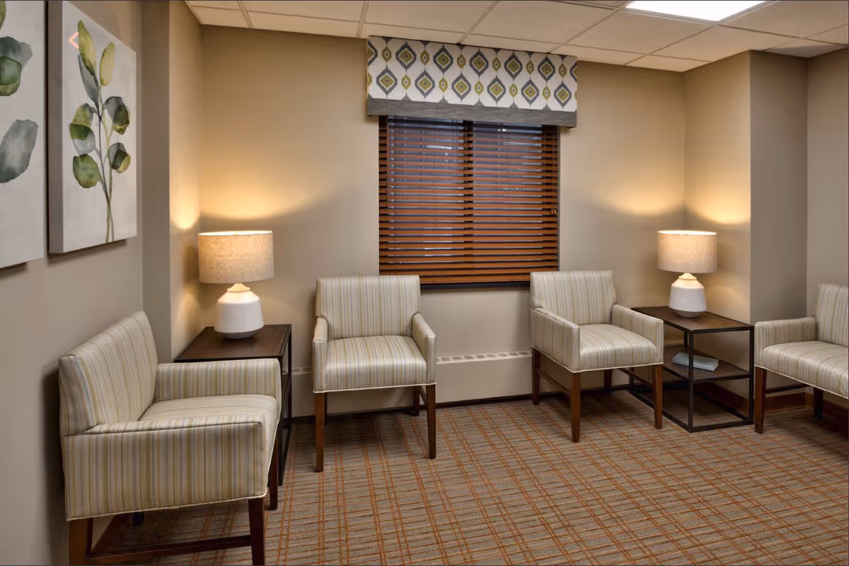 Small seating area with striped armchairs, side tables and lamps in front of a window with wooden blinds.