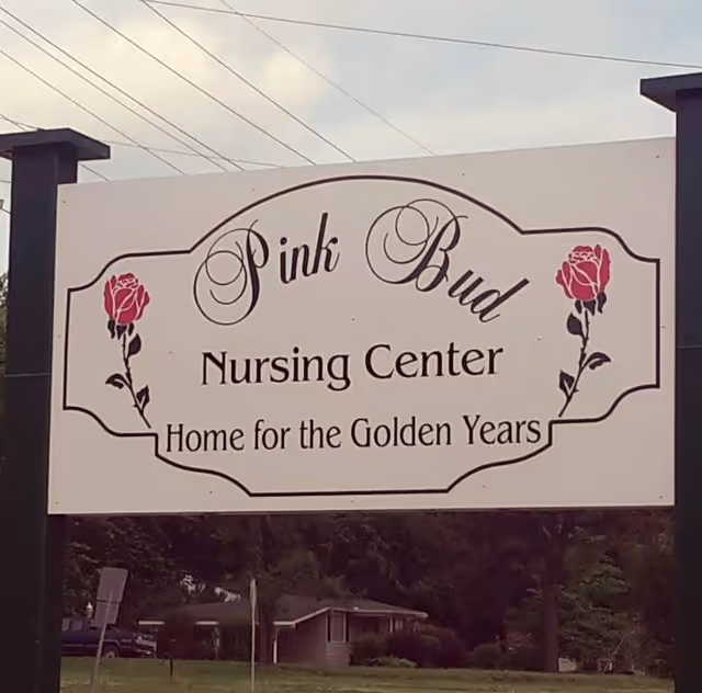Outdoor sign for Pink Bud Nursing Center with decorative pink rose illustrations on each side and the tagline 'Home for the Golden Years'.