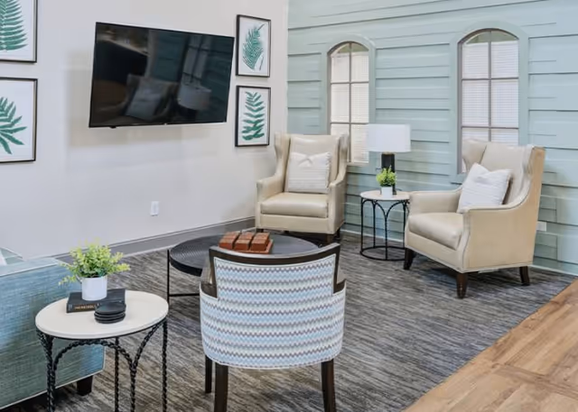 Comfortable communal living area with armchairs, a wall-mounted TV, side tables, and decorative artwork.