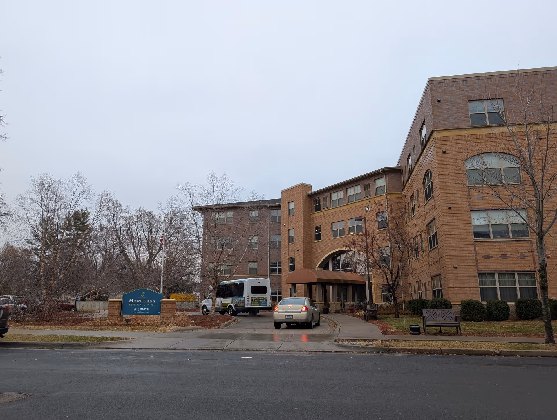 Brick multi-story senior living building entrance with a Minnehaha sign, parked cars and leafless trees in front.