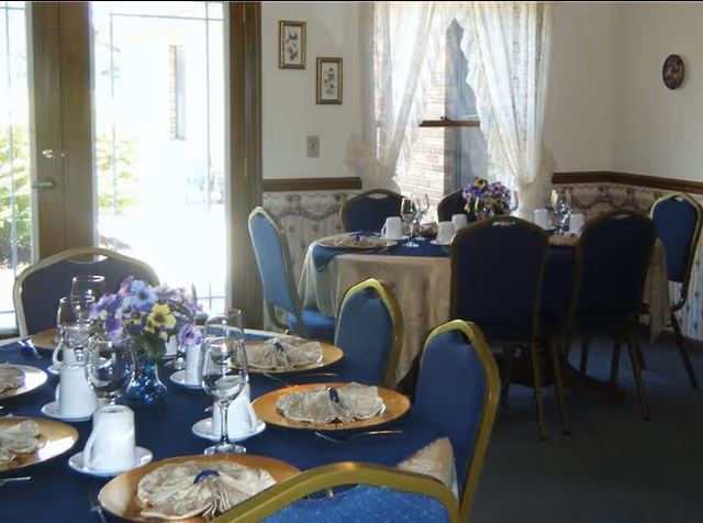 Tables set for a meal in a dining room with blue chairs, place settings, and floral centerpieces.
