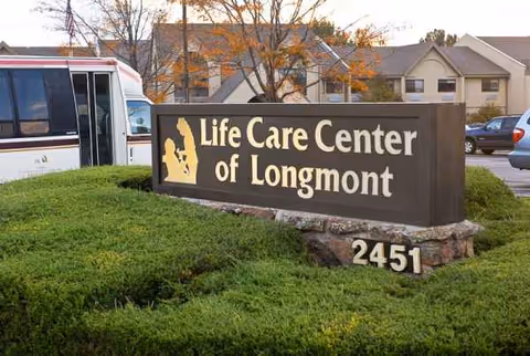 Exterior sign reads Life Care Center of Longmont beside landscaping and a parked bus.