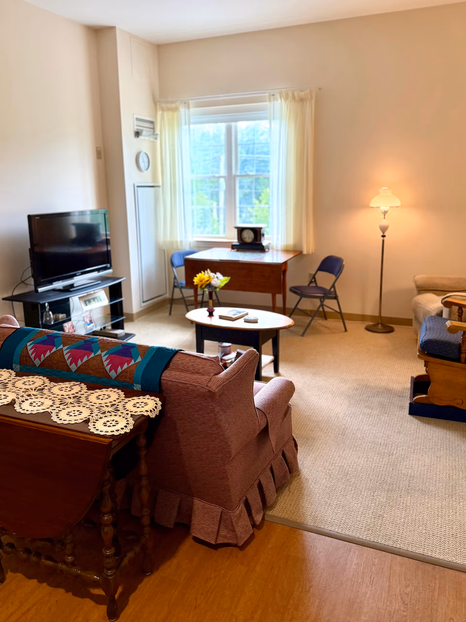 Bright furnished living room with a sofa, TV, coffee table, floor lamp and a small table by a window.