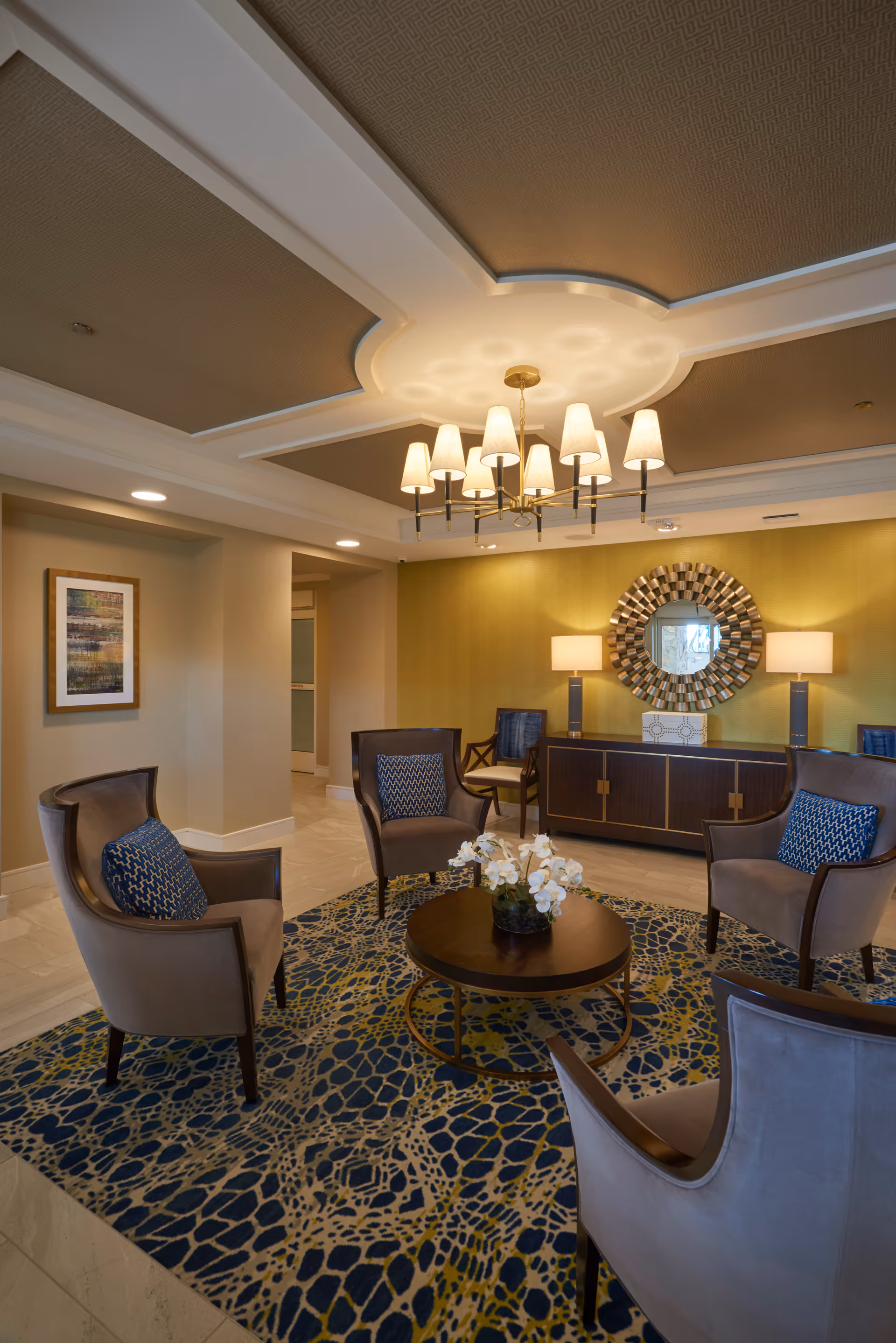 Elegant lounge with a chandelier, circular seating around a central coffee table, and a decorative mirror and sideboard against a green accent wall.