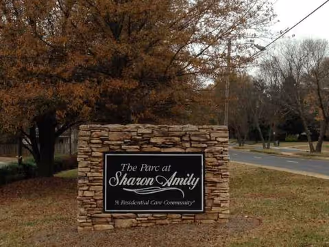 Stone sign displays 'The Parc at Sharon Amity' near a tree-lined street.