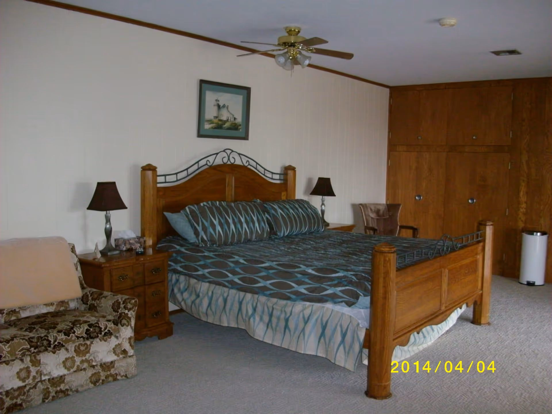Wood-furnished bedroom with a large bed, patterned bedding, bedside tables with lamps, an armchair and built-in wooden closets.