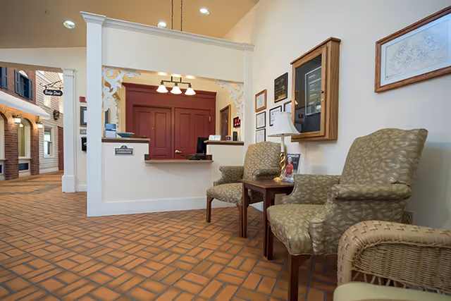 Reception area with a front desk set against red paneled doors and upholstered chairs in a tiled entryway.