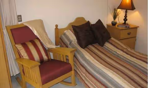 A cozy bedroom with a striped bedspread, wooden chair, nightstand, and lamp.
