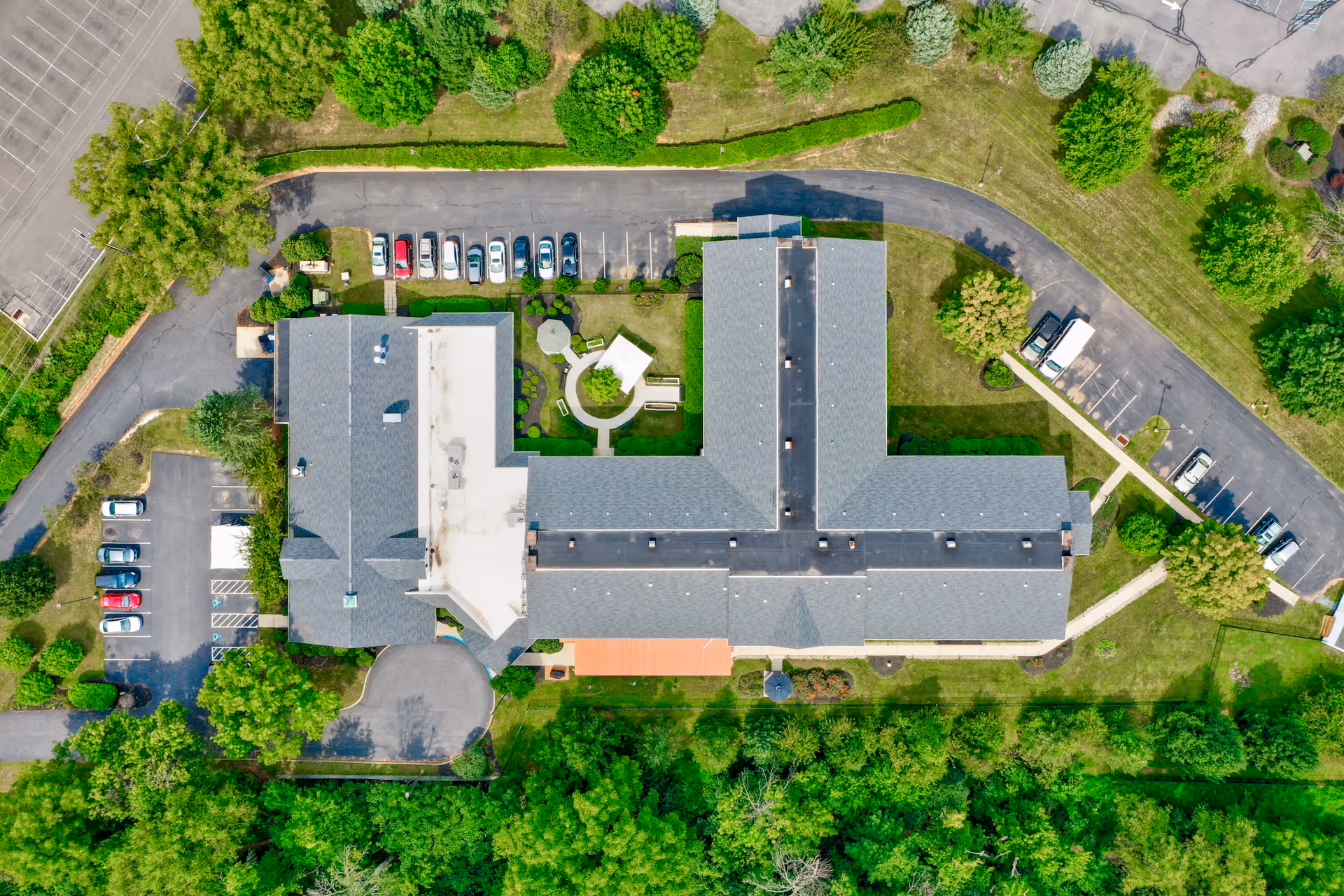 Aerial top-down view of a T-shaped senior living building with parking lots, walkways, and surrounding trees.
