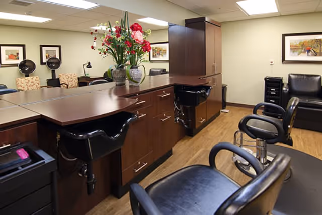 Interior salon area with styling chairs, shampoo sinks, dark wood cabinetry, and a vase of flowers on the counter.