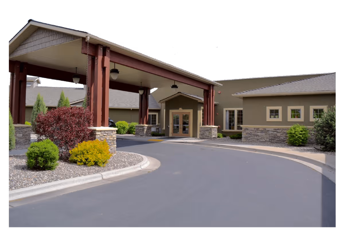 Entrance of Quinn Meadows Rehabilitation and Care Center showing a covered drop-off area with wooden beams and stone pillars, surrounded by landscaped bushes and a curved driveway.