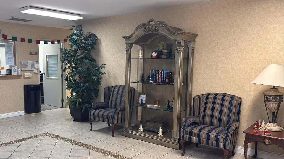 A senior facility reception seating area with two striped armchairs, a glass display cabinet, a potted plant, and a side table with a lamp.