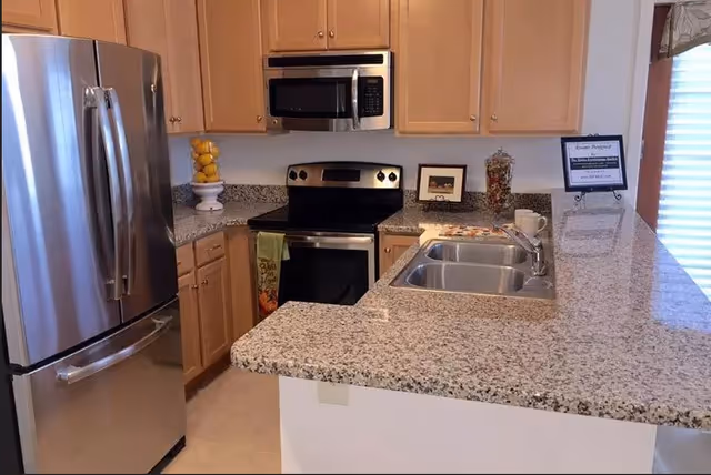 Kitchen with stainless steel refrigerator, stove and microwave, light wood cabinets, granite countertops and a double sink.