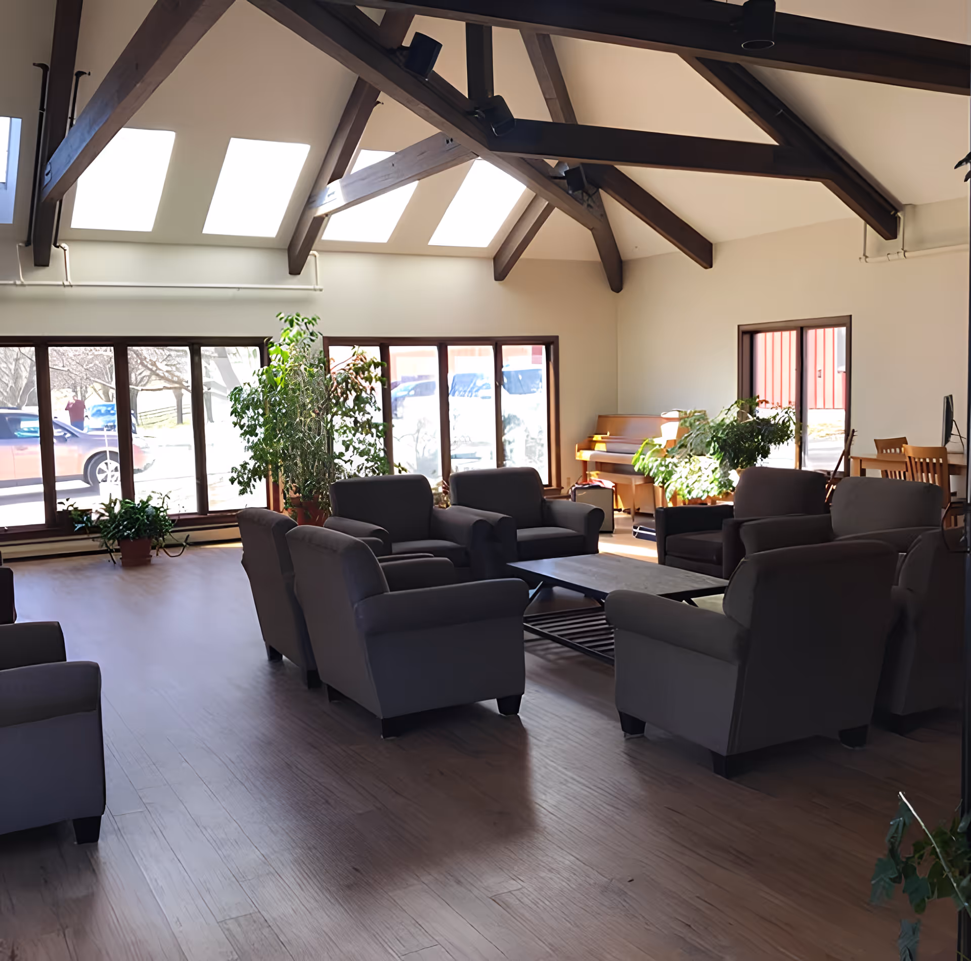 Sunlit communal living room with armchairs arranged around a coffee table, skylights and exposed wooden ceiling beams.