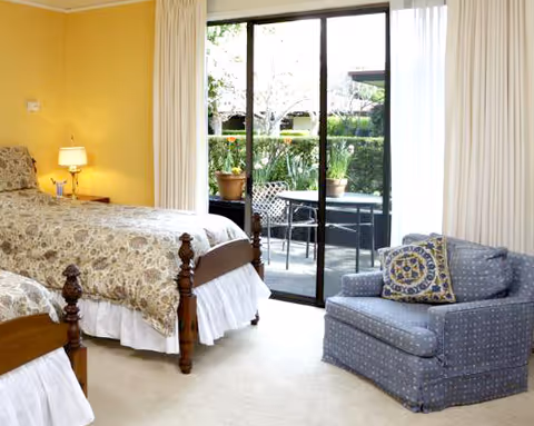 Bedroom with two twin beds, a patterned armchair, and sliding glass doors leading to a small outdoor patio.