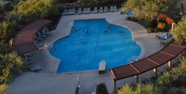 Aerial view of a landscaped outdoor swimming pool with lounge chairs, shaded cabanas, and a few swimmers.