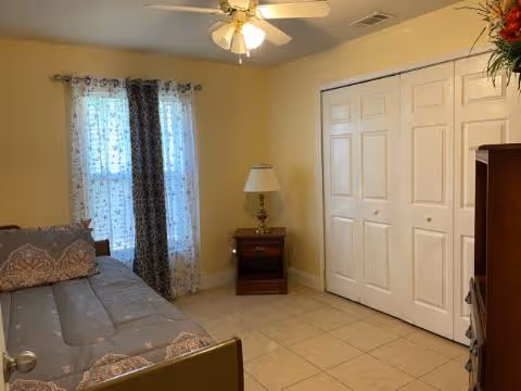Bedroom with a daybed, nightstand and lamp, white closet doors, ceiling fan, and a curtained window.