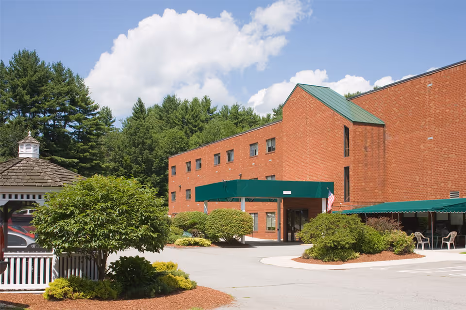 Red brick building front with a green awning entrance, a gazebo, and landscaped shrubs under a blue sky.