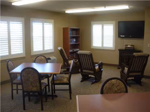 Common lounge area with tables, chairs, recliners, a bookshelf, and a wall-mounted TV.
