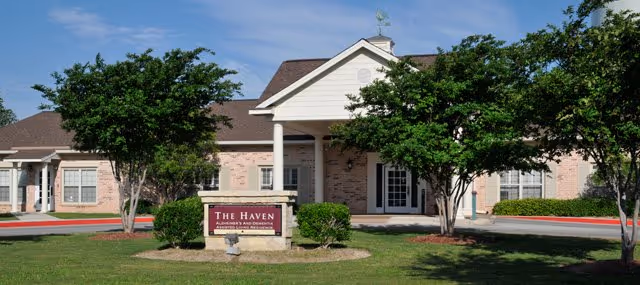 Front exterior view of The Haven in the Summit facility showing a single-story brick building with a covered entrance, surrounded by green trees and a well-maintained lawn under a clear blue sky.