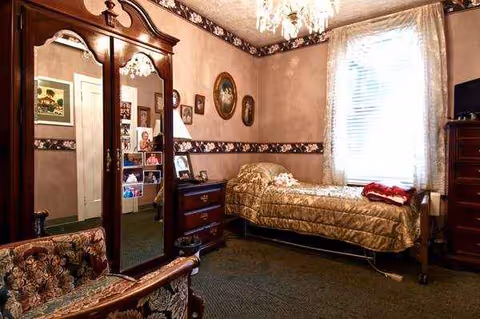 A bedroom with a bed, dresser, mirror, and window in a senior living facility.