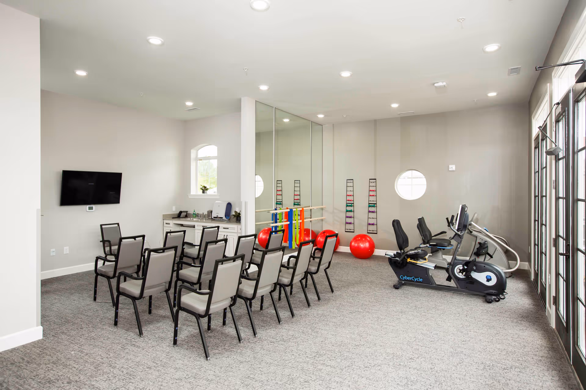Bright activity/fitness room with rows of chairs, exercise bikes, large mirrors and red exercise balls.